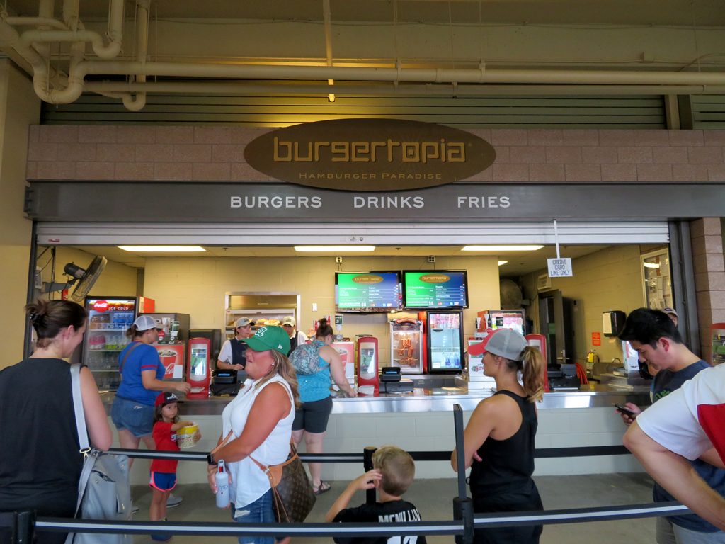 People stand in line in front of a concession stand called "Burgertopia."