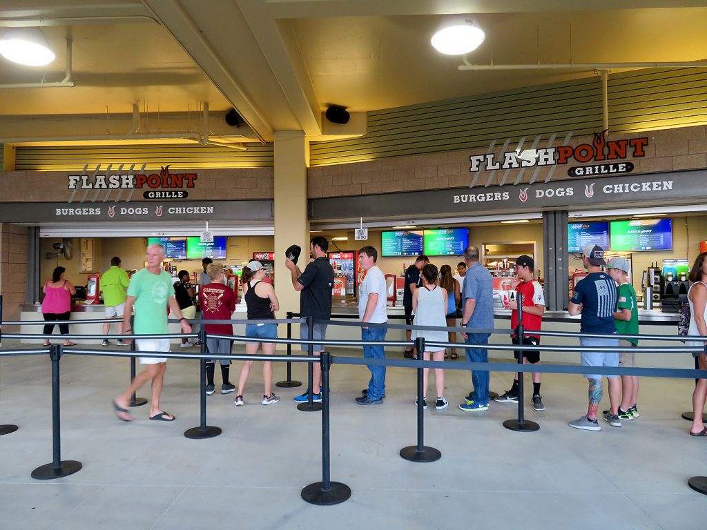 Several people stand in line in front of a concession stand called Flash Point Grille.