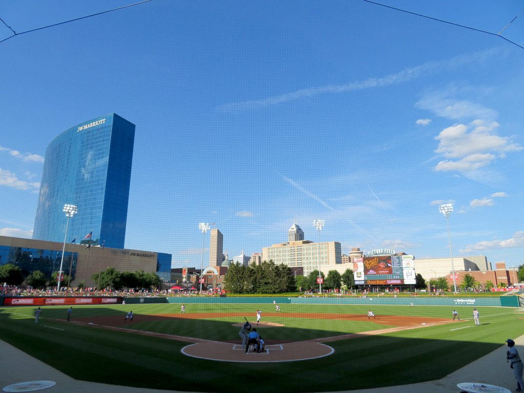 Overview of a baseball field with Indianapolis skyline in the background as pitcher delivers a pitch.