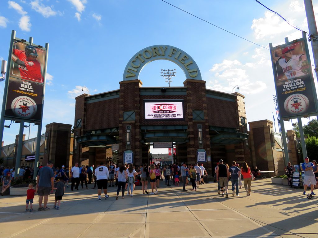 Several people walk toward a large brick structure with "Victory Field" arched above it.
