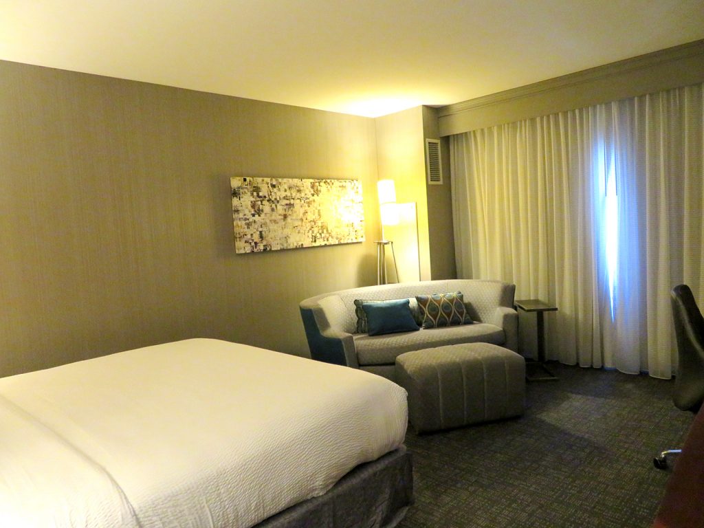 Angled view of hotel room with king-size bed to left and oval sofa in the center.