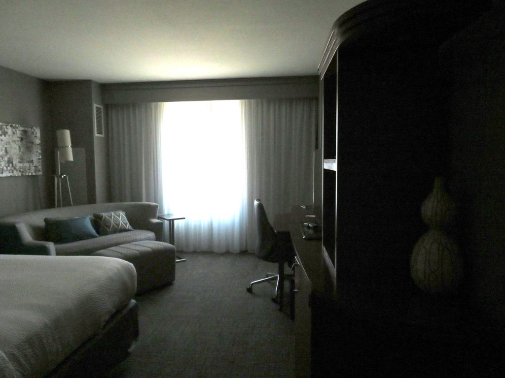 Entrance into hotel room with king-size bed and oval sofa to left and large wooden dresser and desk on the right.