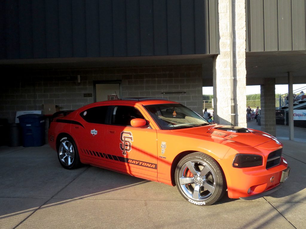 A side view of a San Francisco Giants orange colored 2008 Dodge Charger that is covered with Giants logos.