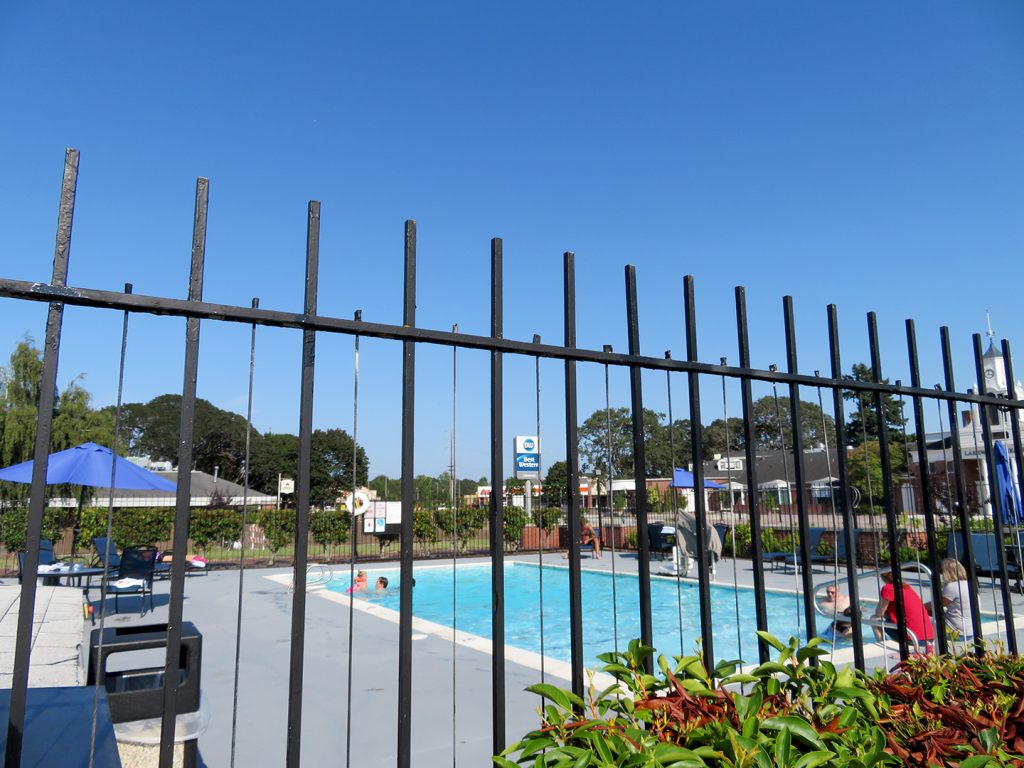 Rectangular outdoor pool with metal fence around it and multiple people swimming in it at the Best Western Lakewood..
