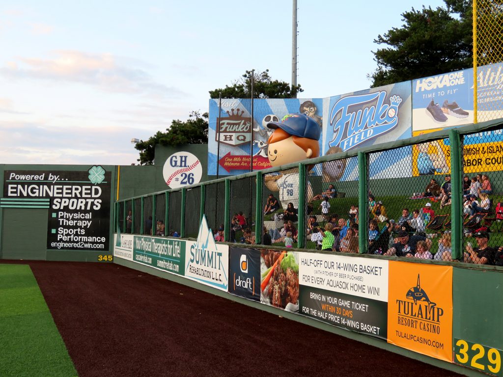 Tall chain-link fence on the right with several ads in front of it, a Freddy Funko statue in the center, and a circular banner with "G.H. #26" written inside it.