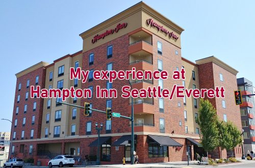 Street corner with a large building and text overlaying image that says "My experience at the Hampton Inn Seattle/Everett."