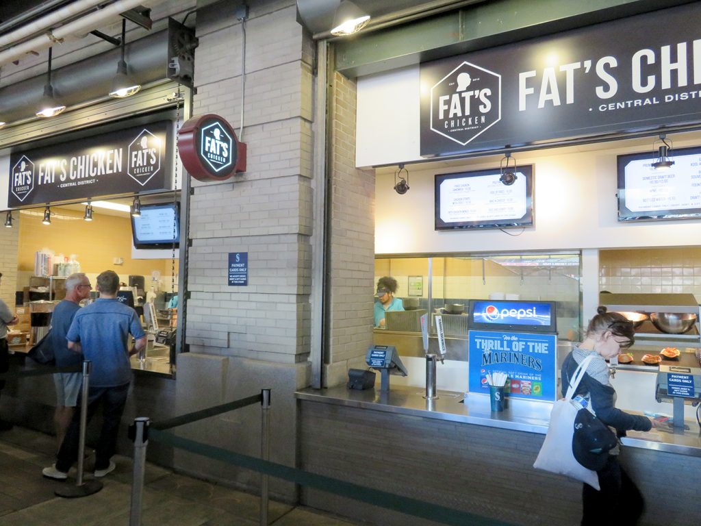 People stand in front of concession stand with a sign that says "Fat's Chicken."