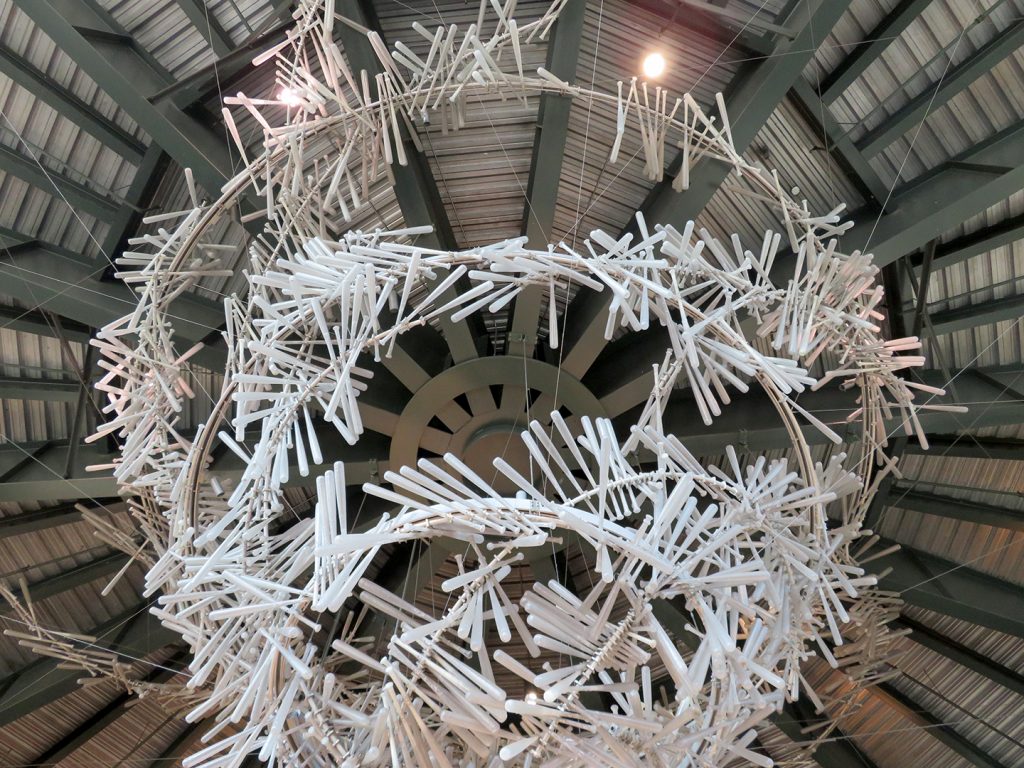 Multiple circles of white resin baseball bats hang from a ceiling mimicking a chandelier.