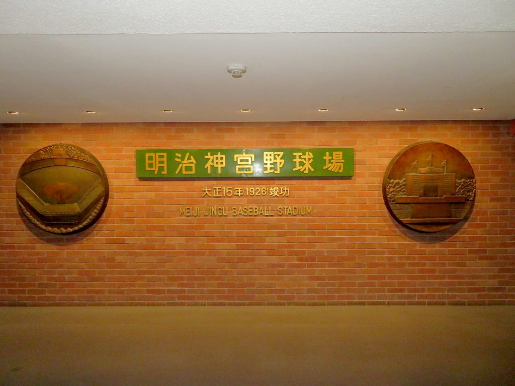 Brick wall with two circular plaques showing the field on the left and the center field tower on the right and text in the middle that says "Meiji Jingu Baseball Stadium."