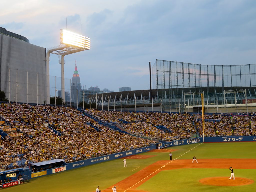 A view from a baseball of a skyscraper in the distance with an oval stadium between the two structures.