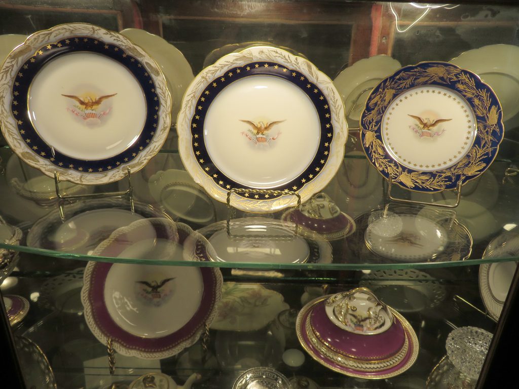 Three china plates with the American presidential seal in the center inside a china cabinet at the Benjamin Harrison Presidential Site.
