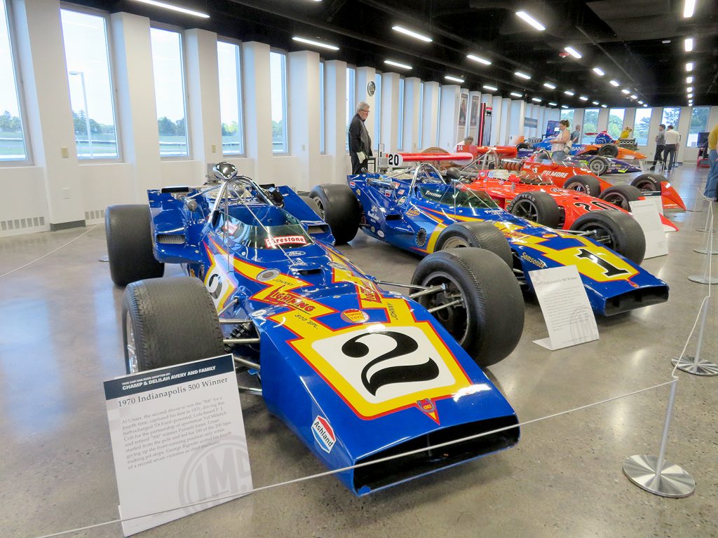 Four Indianapolis 500 winning racecars starting with people walking around the vehicles.