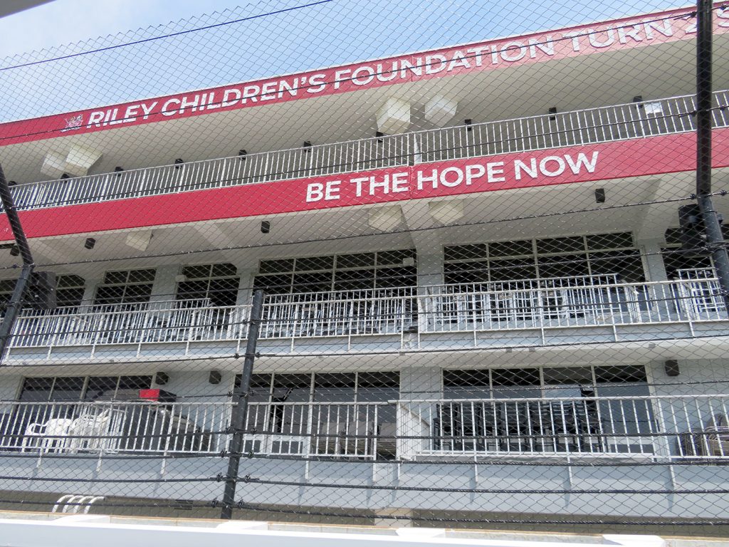 Multiple-floor building with balcony seating behind a fence with signage that says "Riley Children's Foundation Turn 2 Suites."