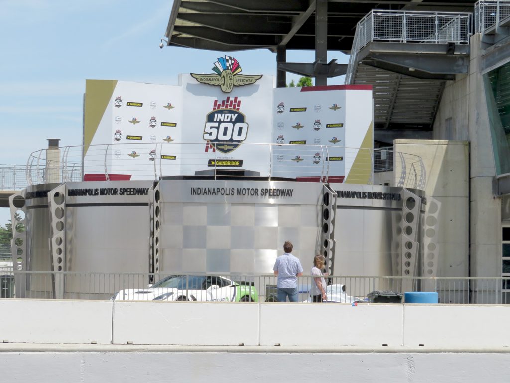 Large oval stand with signage behind it with Indianapolis Motor Speedway logo and "Indy 500" written on it.
