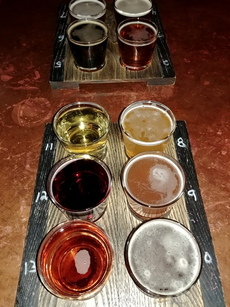 A vertical image of two six-glass tasting trays of beer.