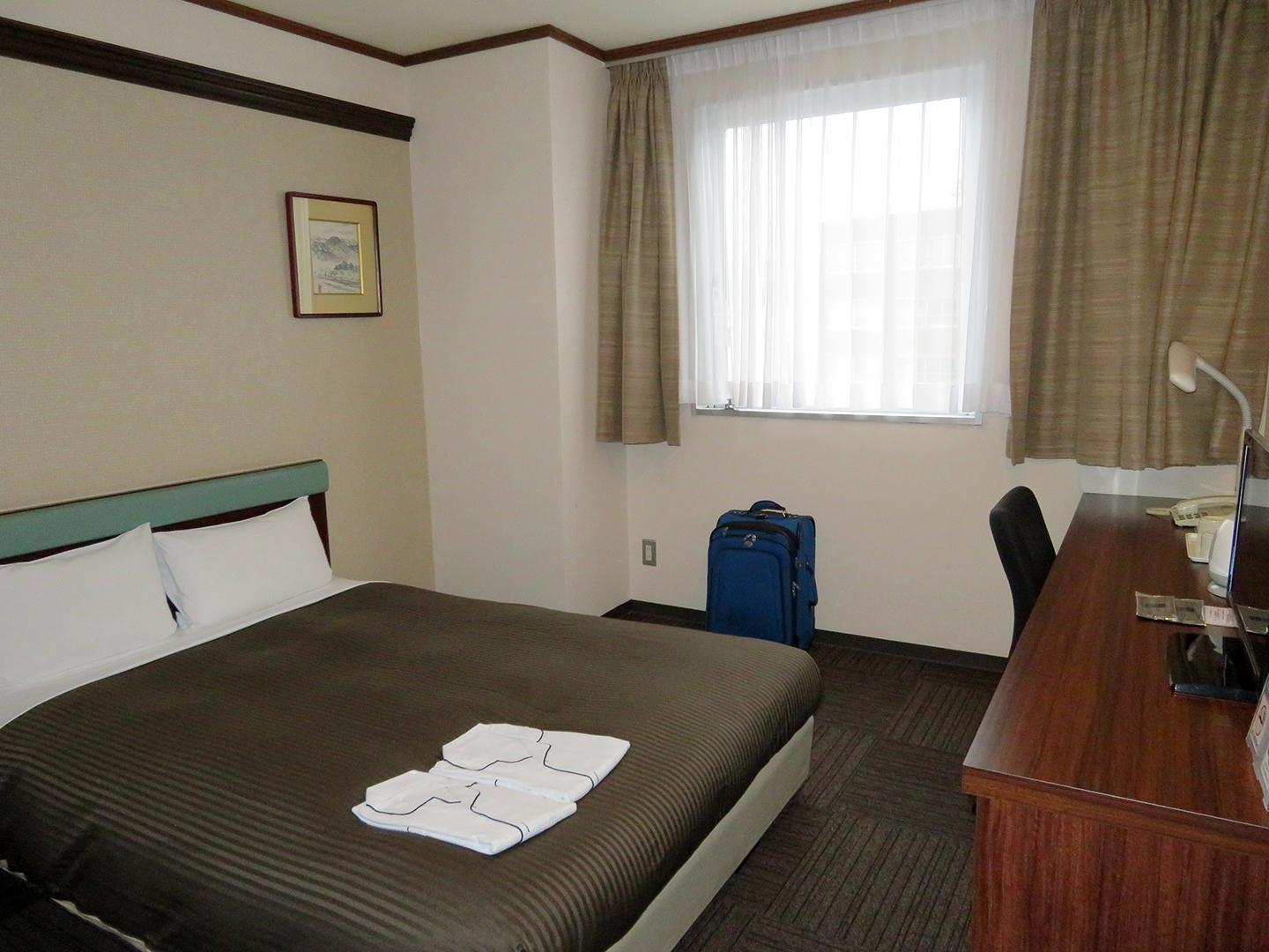 Overview of double room at Hotel Matsumoto Yorozuya with bed to the left and desk to the right.